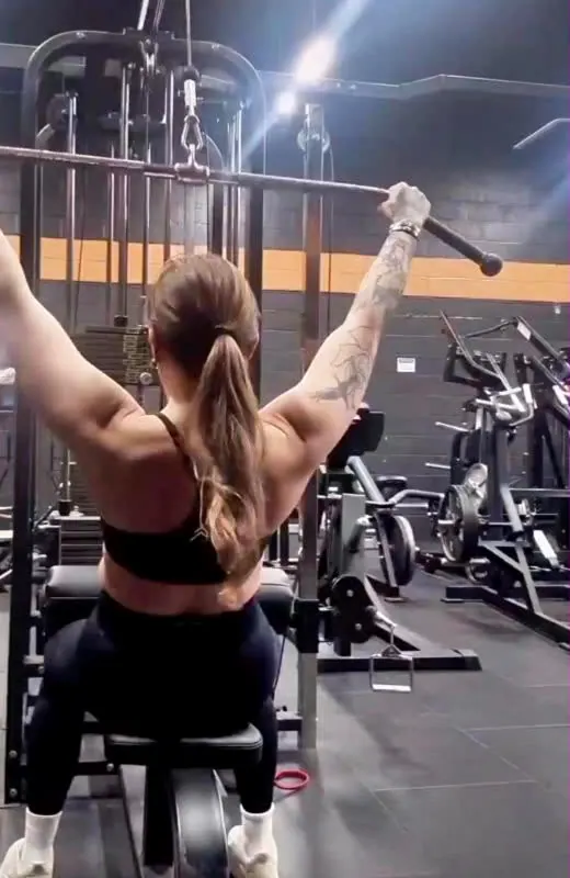 Fiona doing a lat pulldown in the gym, seen from behind